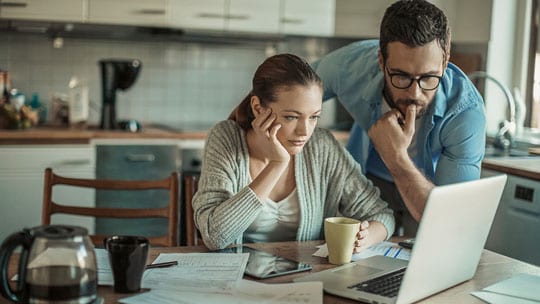 A young couple studies a laptop screen.
